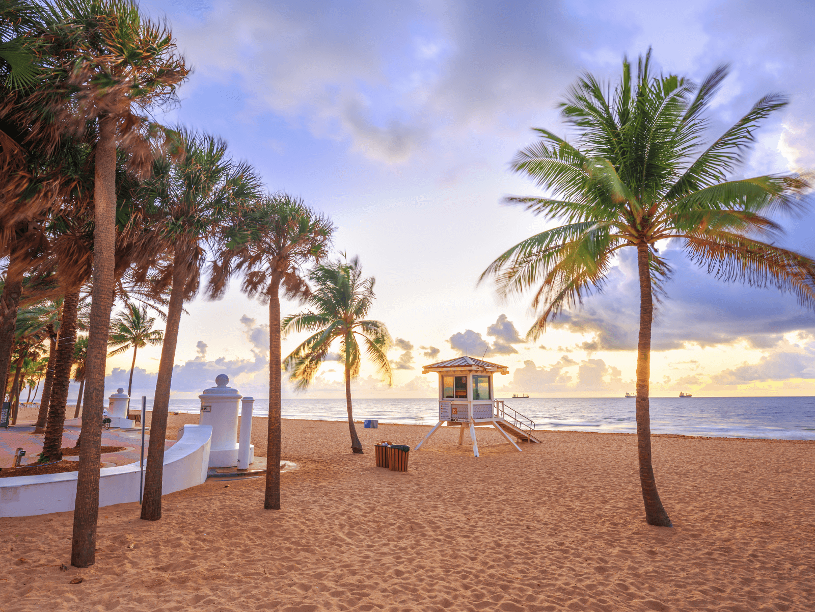 A picture of the beach in Palm Coast at sunset. There are palm trees and a lifeguard station is centered in the photo.