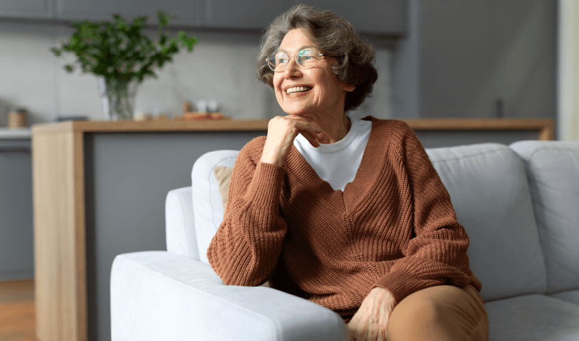 An older woman with grey hair is posing with her hand under her chin and looking off camera